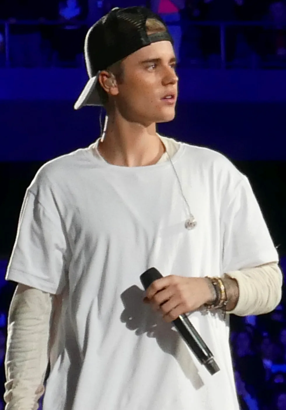 Justin Bieber cantando en un concierto en 2015, con gorra hacia atrás y micrófono en la mano
